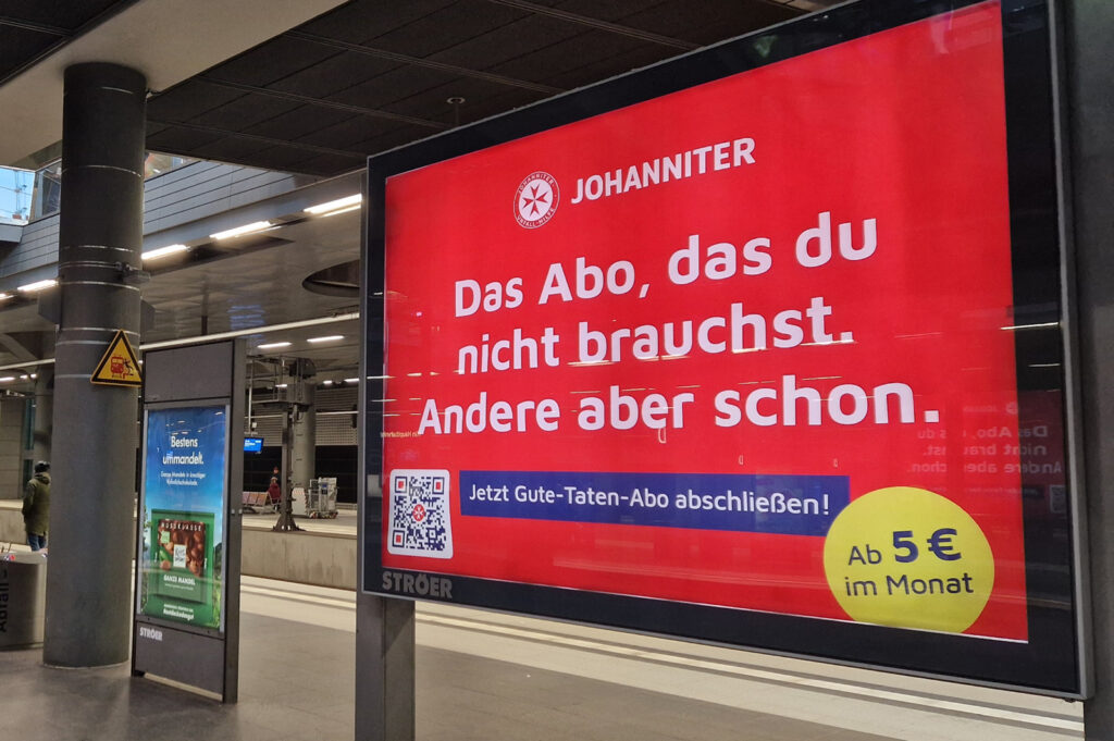 Werbetafel am Bahnhof für das Gute-Taten-Abo der Johanniter